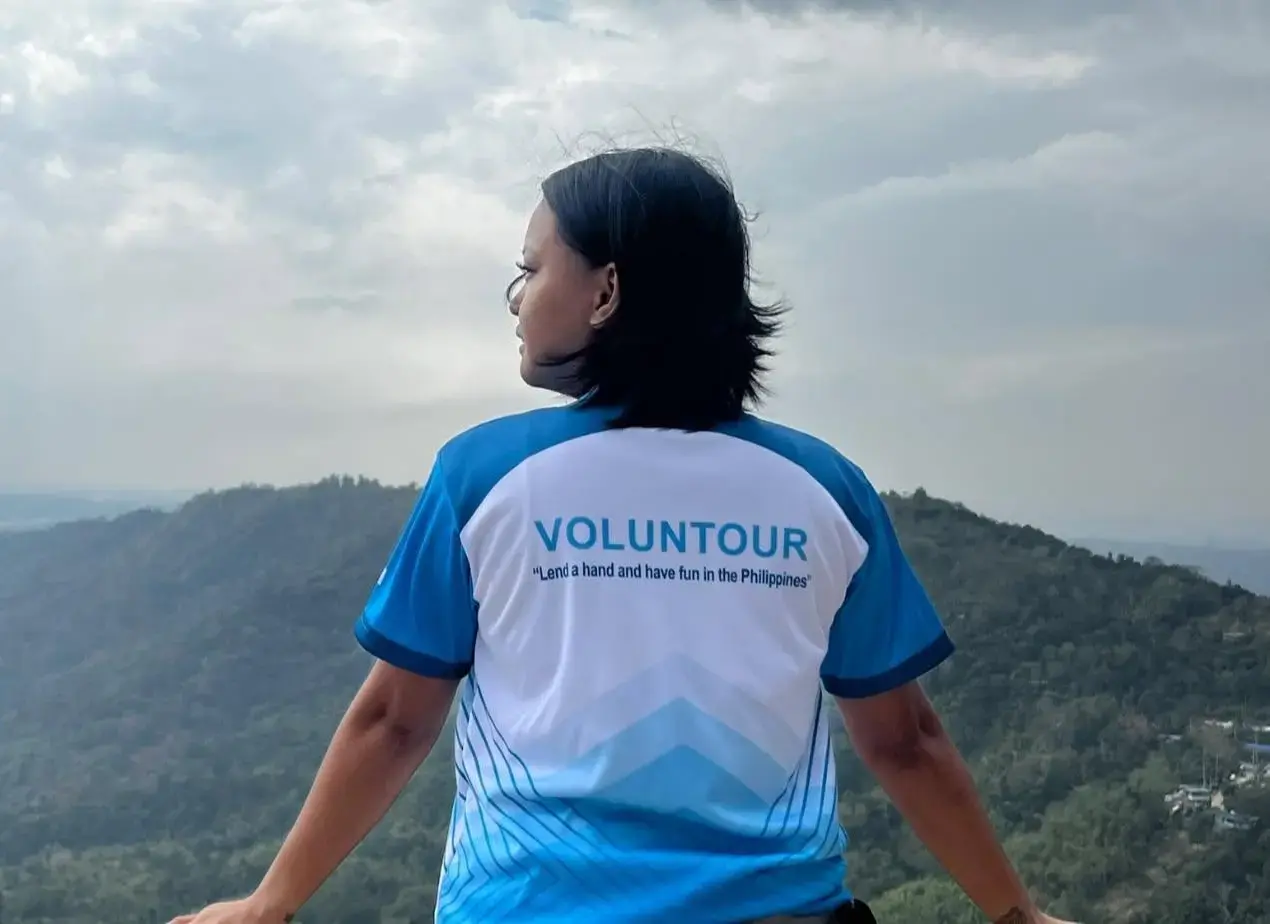 Voluntour team member wearing a blue and white shirt with logo, overlooking a scenic mountain landscape.