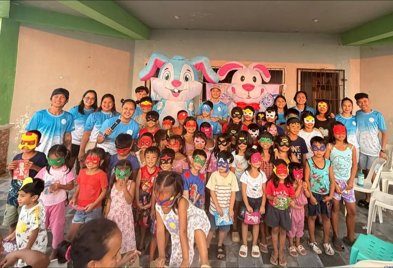 Adults and children posing together indoors with large pink and white balloon decorations during a Voluntour Philippines community gathering.